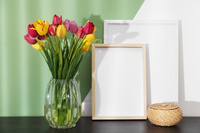 Photo of Bouquet of beautiful tulips and frames on table near color wall