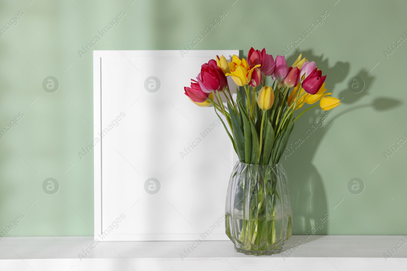 Photo of Bouquet of beautiful tulips and frame on table near color wall
