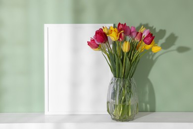 Photo of Bouquet of beautiful tulips and frame on table near color wall