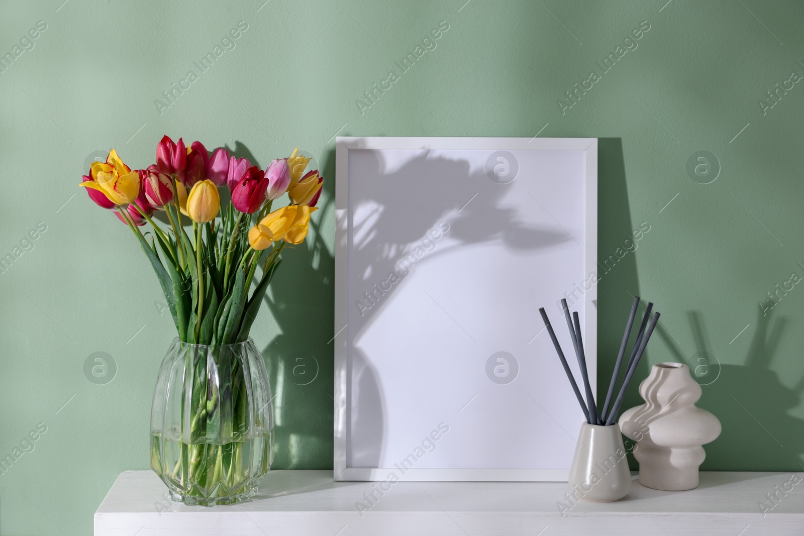 Photo of Bouquet of beautiful tulips and decor on table near color wall