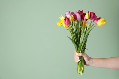 Photo of Woman with bouquet of beautiful tulips on green background, closeup. Space for text