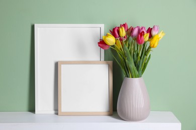 Photo of Bouquet of beautiful tulips and frames on table near color wall