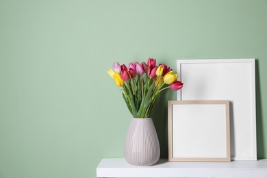 Photo of Bouquet of beautiful tulips and frames on table near color wall. Space for text