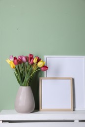 Photo of Bouquet of beautiful tulips and frames on table near color wall. Space for text