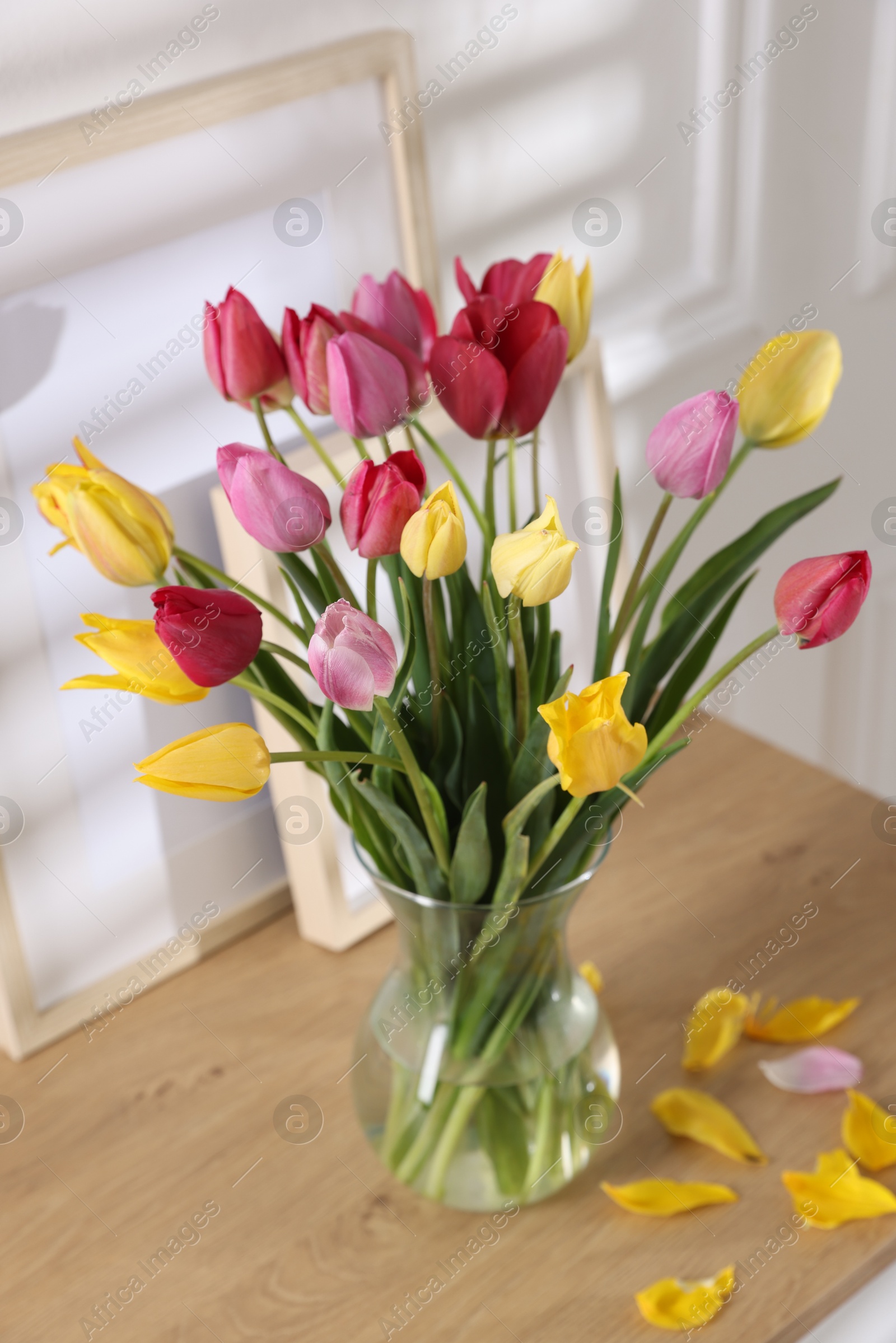 Photo of Bouquet of beautiful tulips and frames on wooden table indoors