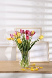 Photo of Bouquet of beautiful tulips and frames on wooden table indoors. Space for text