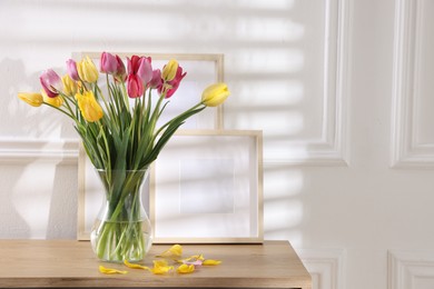Photo of Bouquet of beautiful tulips and frames on wooden table indoors. Space for text