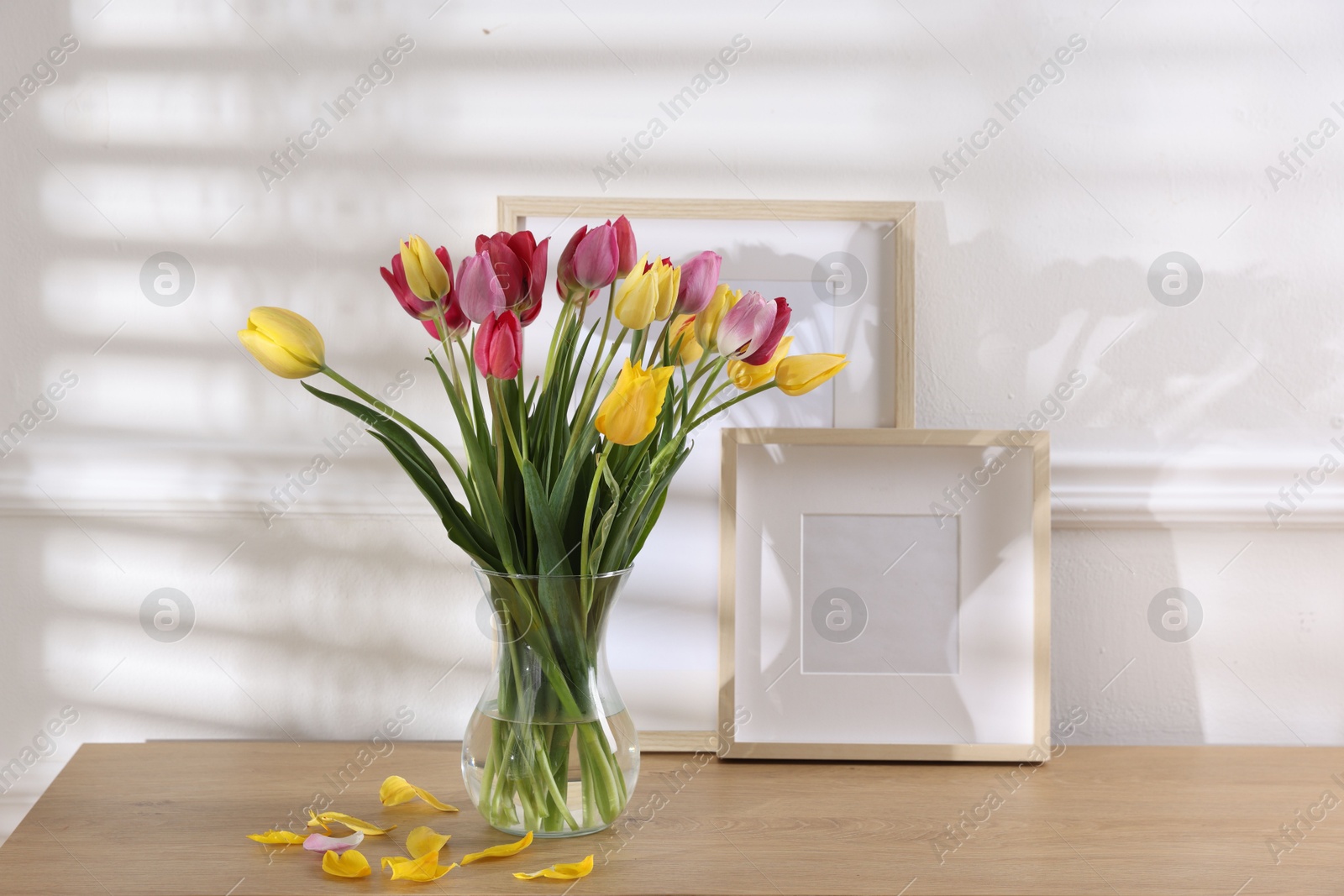 Photo of Bouquet of beautiful tulips and frames on wooden table indoors