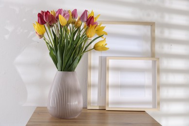 Photo of Bouquet of beautiful tulips and frames on wooden table indoors