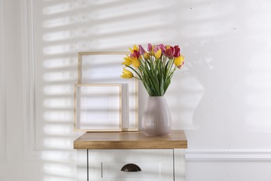 Photo of Bouquet of beautiful tulips and frames on wooden table indoors