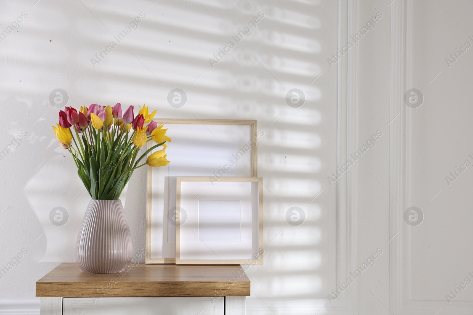 Photo of Bouquet of beautiful tulips and frames on wooden table indoors. Space for text