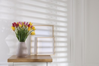 Photo of Bouquet of beautiful tulips and frames on wooden table indoors. Space for text