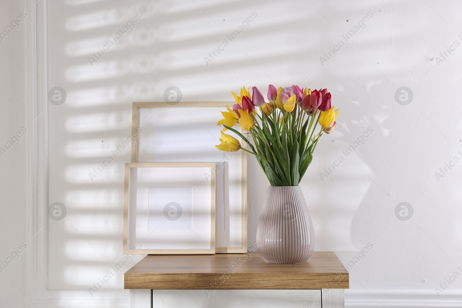 Photo of Bouquet of beautiful tulips and frames on wooden table indoors