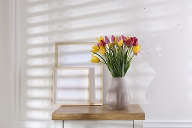 Photo of Bouquet of beautiful tulips and frames on wooden table indoors