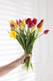 Photo of Woman with bouquet of beautiful tulips near white wall, closeup