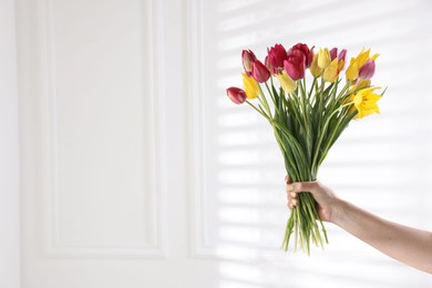 Photo of Woman with bouquet of beautiful tulips near white wall, closeup. Space for text