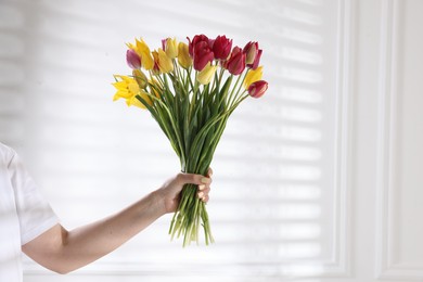 Photo of Woman with bouquet of beautiful tulips near white wall, closeup