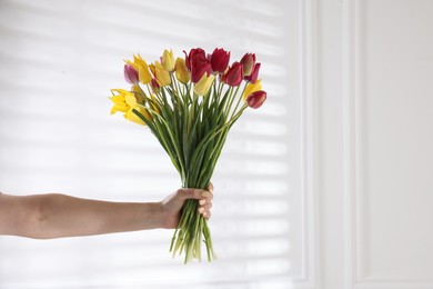 Photo of Woman with bouquet of beautiful tulips near white wall, closeup