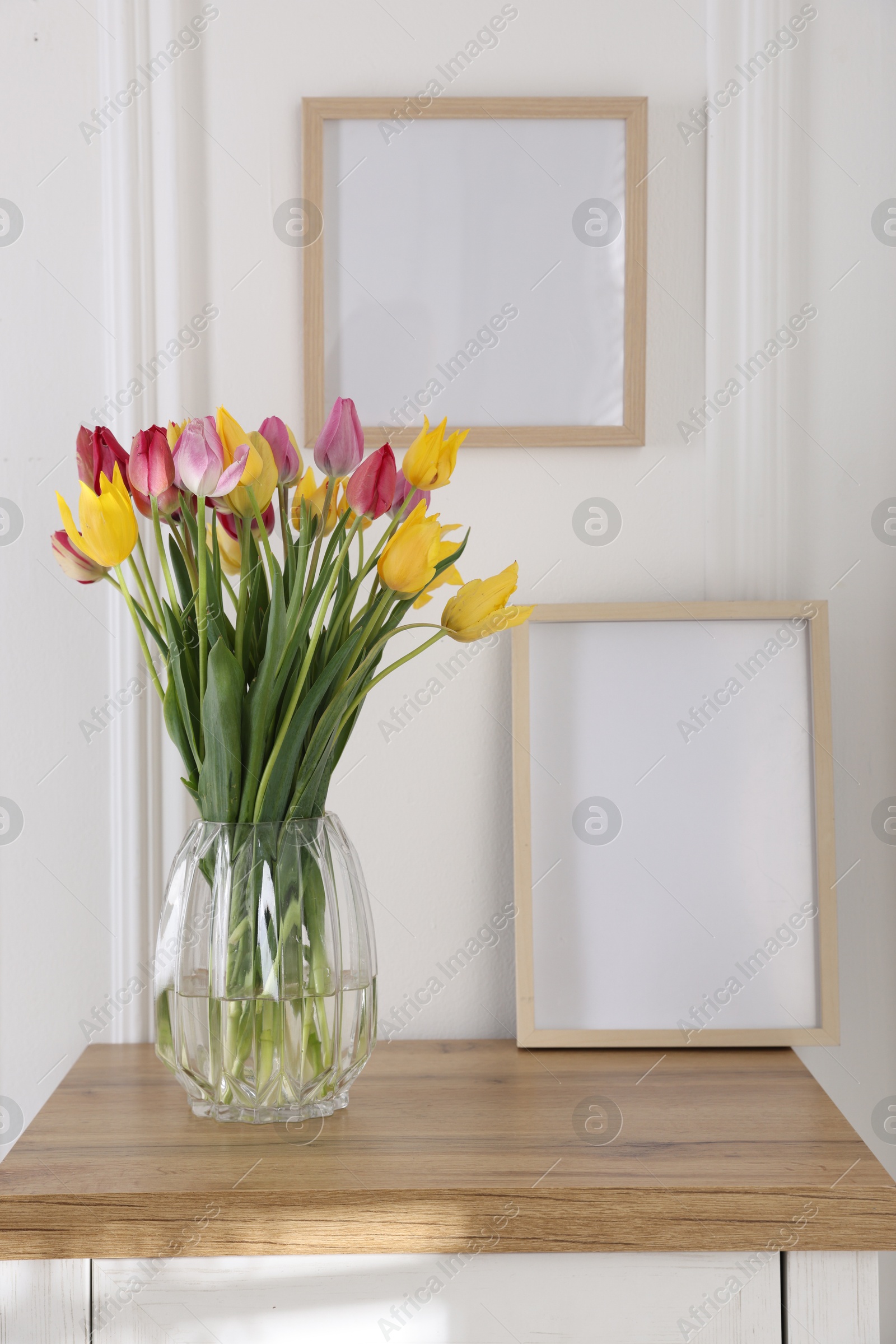 Photo of Bouquet of beautiful tulips and frame on wooden table indoors