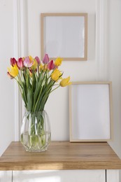 Photo of Bouquet of beautiful tulips and frame on wooden table indoors