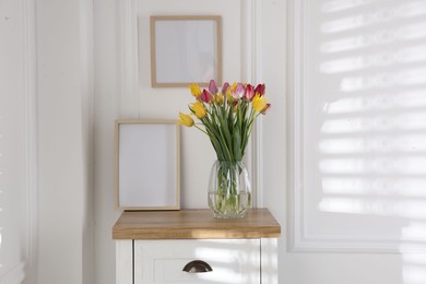 Photo of Bouquet of beautiful tulips and frame on wooden table indoors