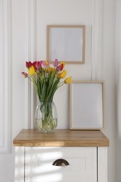 Photo of Bouquet of beautiful tulips and frame on wooden table indoors