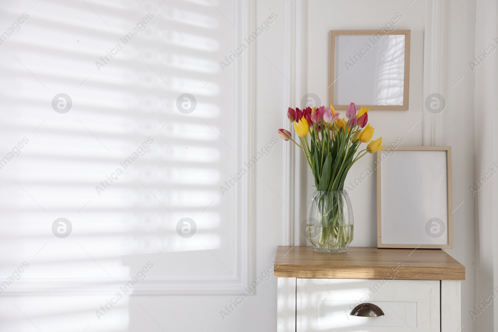 Photo of Bouquet of beautiful tulips and frame on wooden table indoors. Space for text