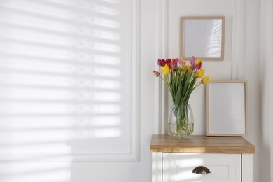 Photo of Bouquet of beautiful tulips and frame on wooden table indoors. Space for text