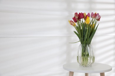 Photo of Bouquet of beautiful tulips on table near white wall. Space for text