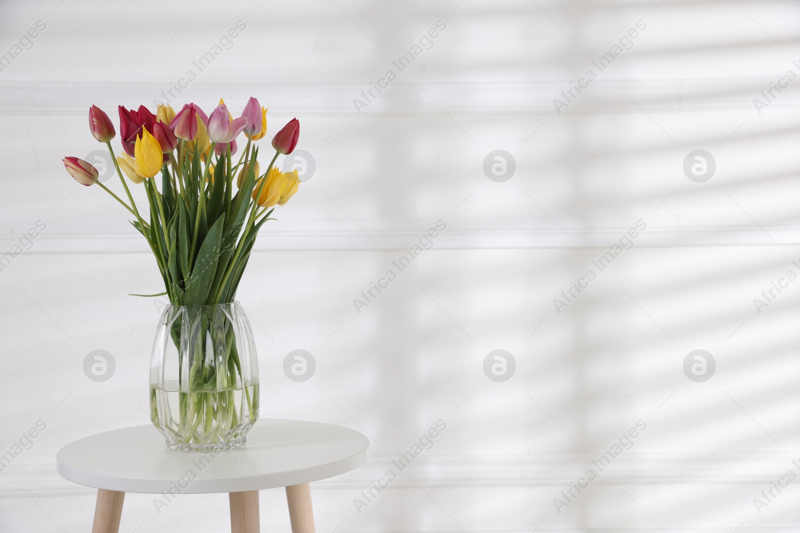 Bouquet of beautiful tulips on table near white wall. Space for text Photo of Bouquet of beautiful tulips on table near white wall. Space for text
