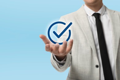 Image of Approved. Man holding virtual check mark in hand on light blue background, closeup