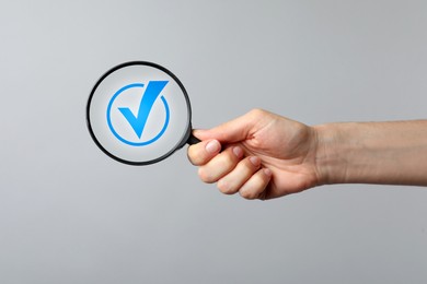 Image of Approved. Woman holding magnifying glass with check mark inside on grey background, closeup