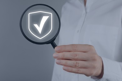 Image of Approved. Woman holding magnifying glass with check mark inside on grey background, closeup