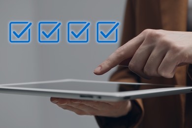 Image of Approved. Woman using tablet on grey background, closeup. Check marks above device