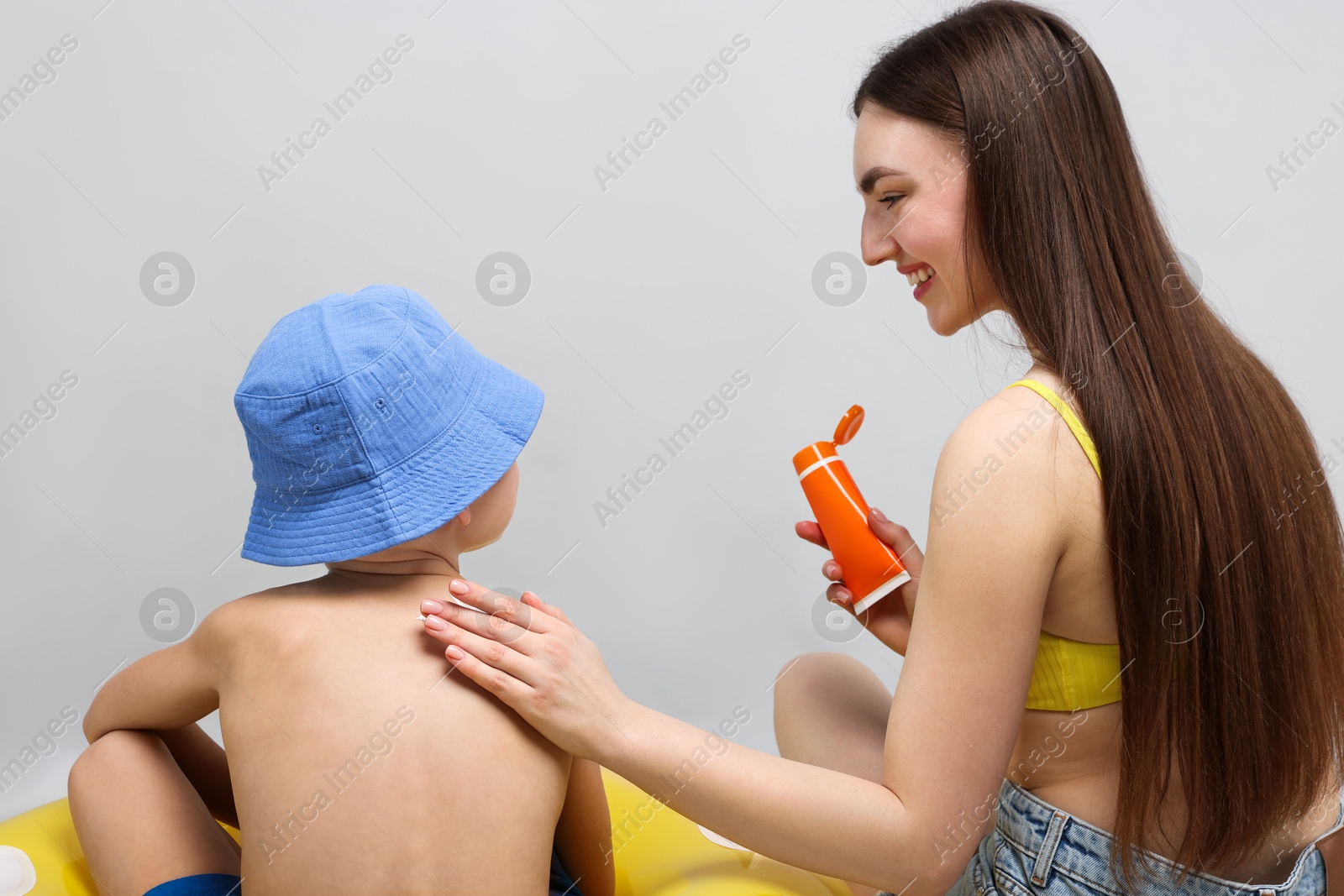 Mother applying sun protection cream onto her son's skin on light grey background Photo of Mother applying sun protection cream onto her son's skin on light grey background