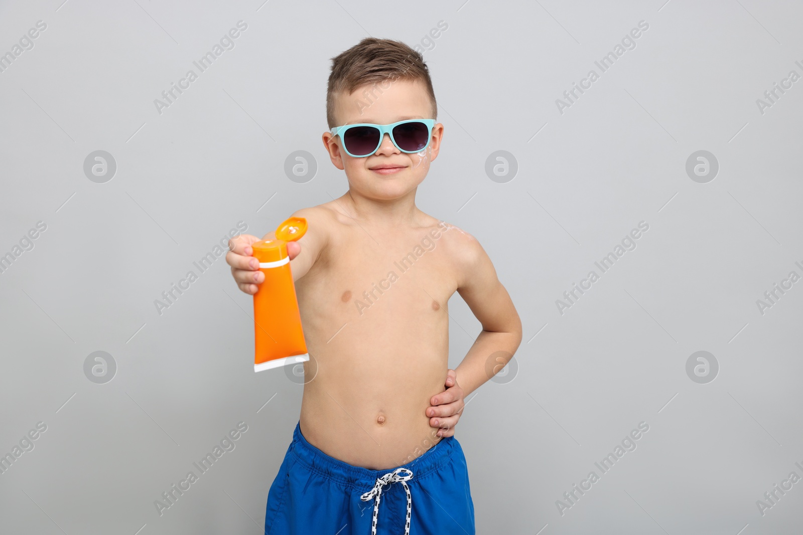 Little boy with tube of sun protection cream on light grey background Photo of Little boy with tube of sun protection cream on light grey background