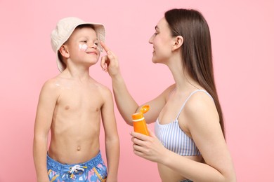 Photo of Mother applying sun protection cream onto her son's skin on pink background