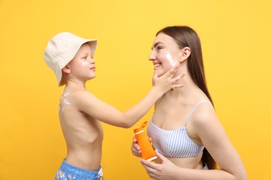 Photo of Son applying sun protection cream onto his mother's skin on yellow background