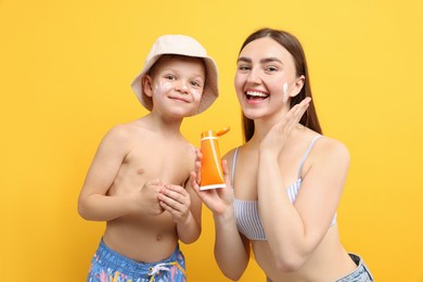 Photo of Mother with sun protection cream and her son on yellow background