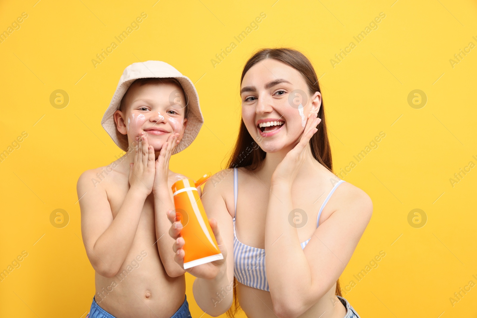 Mother with sun protection cream and her son on yellow background Photo of Mother with sun protection cream and her son on yellow background