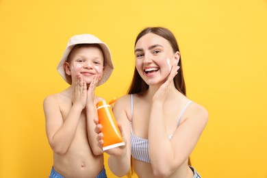 Photo of Mother with sun protection cream and her son on yellow background