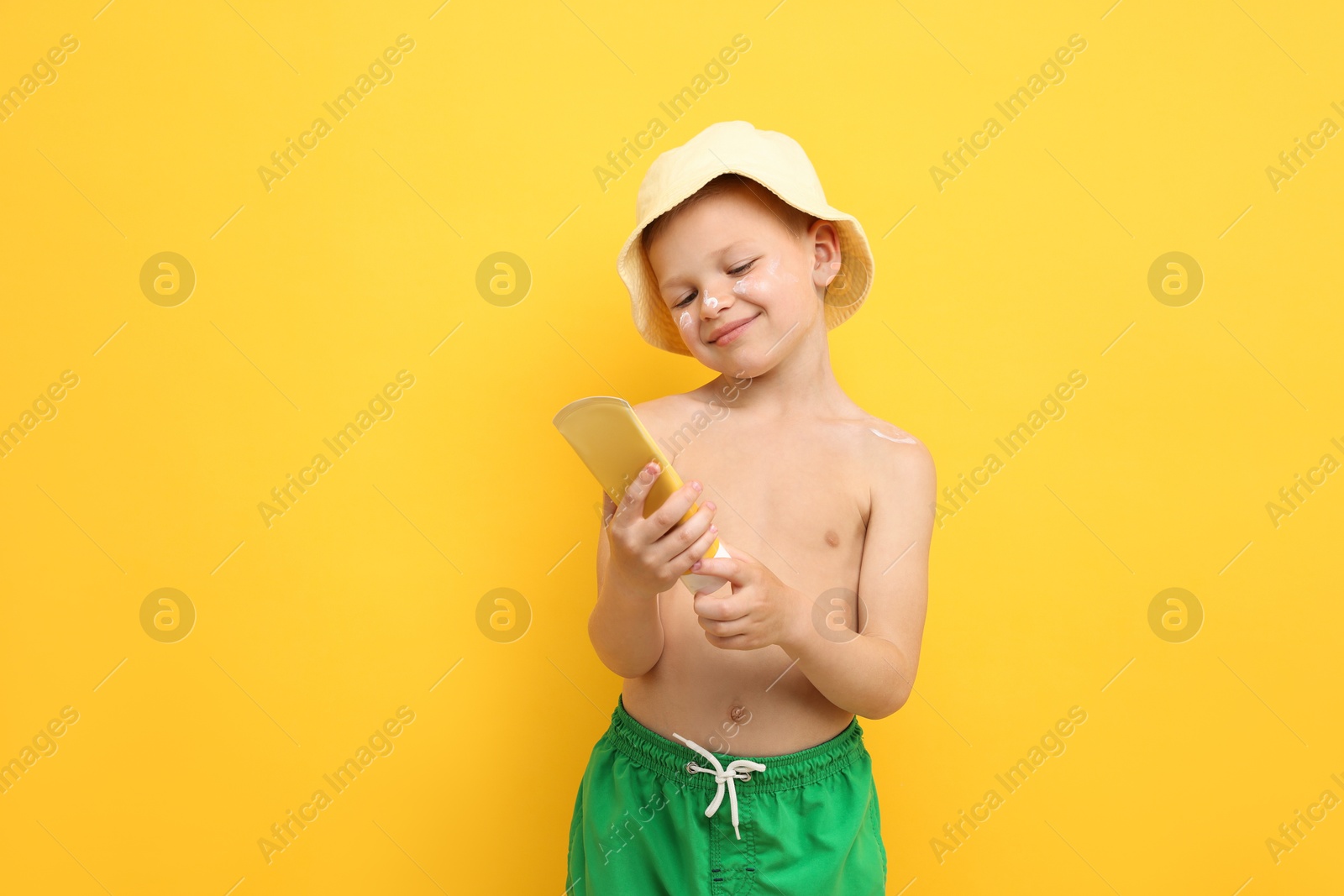 Little boy with tube of sun protection cream on yellow background, space for text Photo of Little boy with tube of sun protection cream on yellow background, space for text