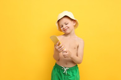 Photo of Little boy with tube of sun protection cream on yellow background, space for text