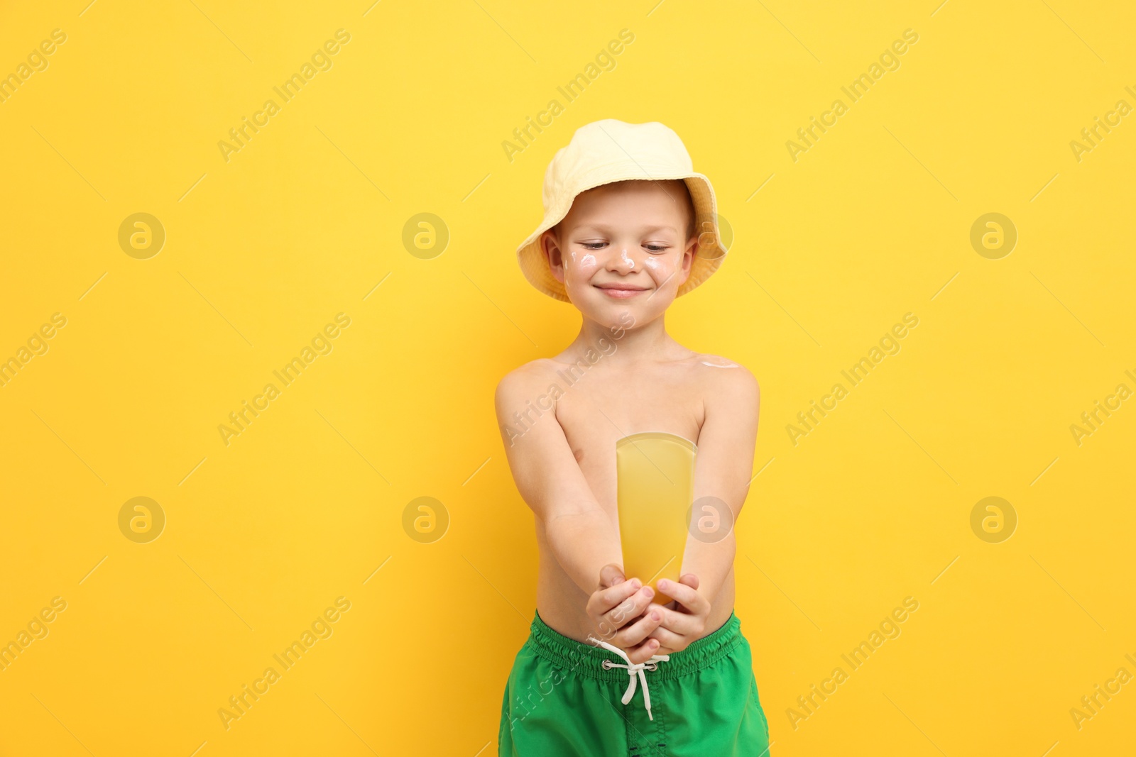 Little boy with tube of sun protection cream on yellow background, space for text Photo of Little boy with tube of sun protection cream on yellow background, space for text