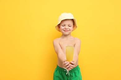 Photo of Little boy with tube of sun protection cream on yellow background, space for text
