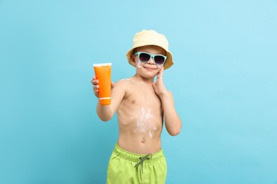 Photo of Little boy with tube of sun protection cream on light blue background
