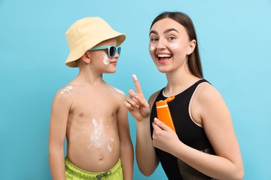 Photo of Emotional mother with sun protection cream and her son on light blue background