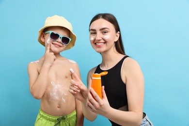 Photo of Mother with sun protection cream and her son on light blue background