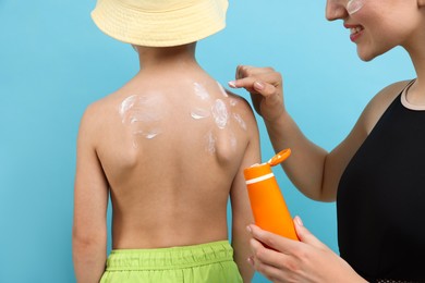 Photo of Mother applying sun protection cream onto her son's skin on light blue background, closeup