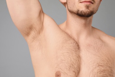 Photo of Young man showing hairy armpit on light grey background, closeup. Epilation procedure